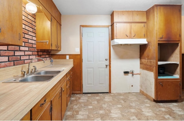 kitchen featuring a wainscoted wall, a sink, light countertops, stone finish flooring, and brown cabinetry