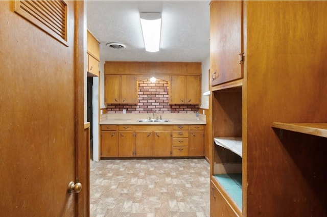 kitchen with brown cabinets, decorative backsplash, light countertops, and a sink