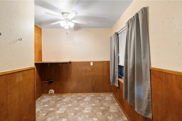 laundry area featuring a ceiling fan, a wainscoted wall, and wood walls