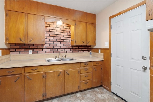 kitchen featuring a wainscoted wall, light countertops, brown cabinetry, a sink, and wooden walls