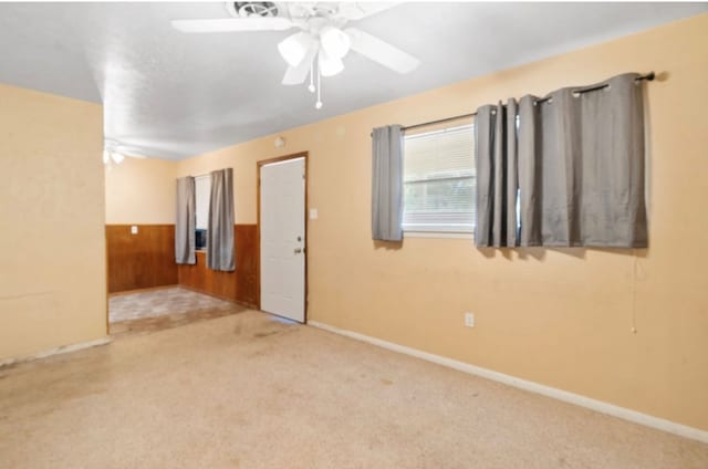 empty room with light carpet, a wainscoted wall, ceiling fan, and wood walls