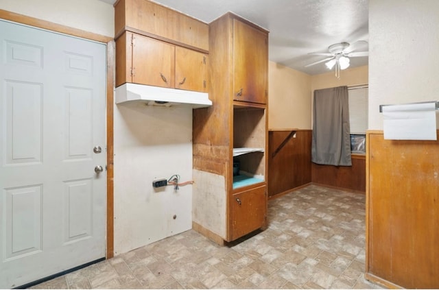 kitchen with a wainscoted wall, light countertops, brown cabinetry, ceiling fan, and wooden walls