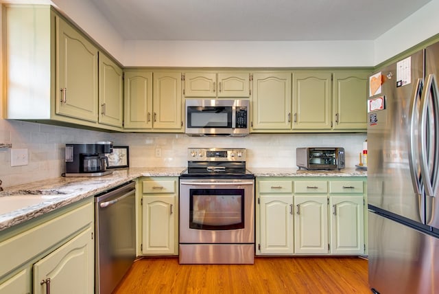 10903 E County Rd 105, Midland, TX 79706 - kitchen with stainless steel appliances, green cabinetry, light wood finished floors, and decorative backsplash