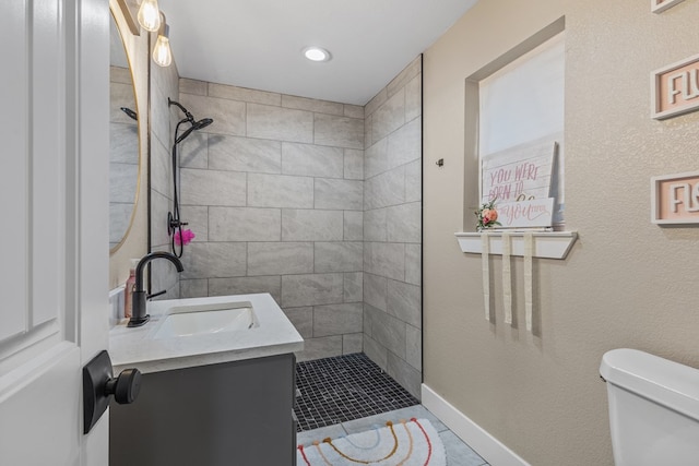 bathroom featuring toilet, baseboards, tiled shower, and vanity