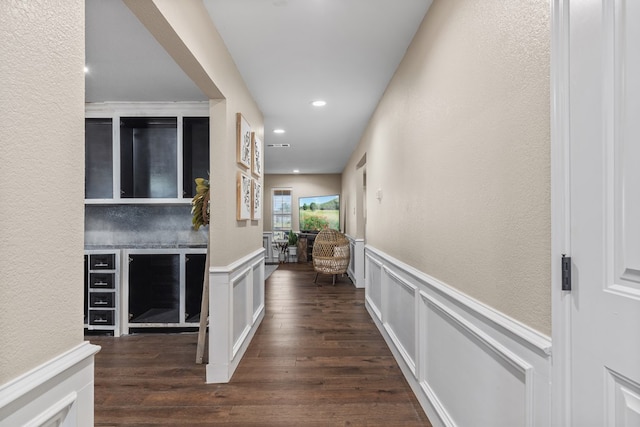 corridor featuring a textured wall, wainscoting, dark wood-style flooring, a decorative wall, and recessed lighting