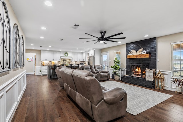 living room with recessed lighting, a brick fireplace, visible vents, and dark wood-style flooring