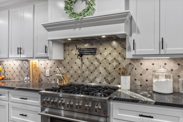 kitchen with dark stone countertops, high end stove, white cabinetry, and custom range hood