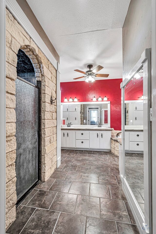 10500 E County Rd 90, Midland, TX 79706 - bathroom with double vanity, ceiling fan, a textured ceiling, a shower stall, and stone tile floors