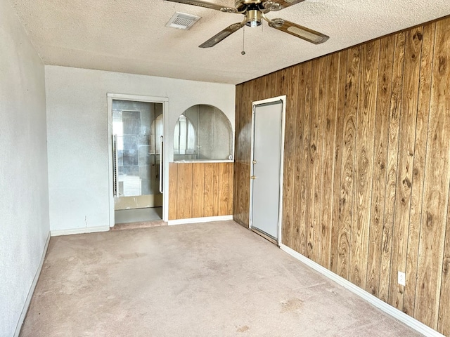 carpeted spare room with ceiling fan, a textured ceiling, and wooden walls