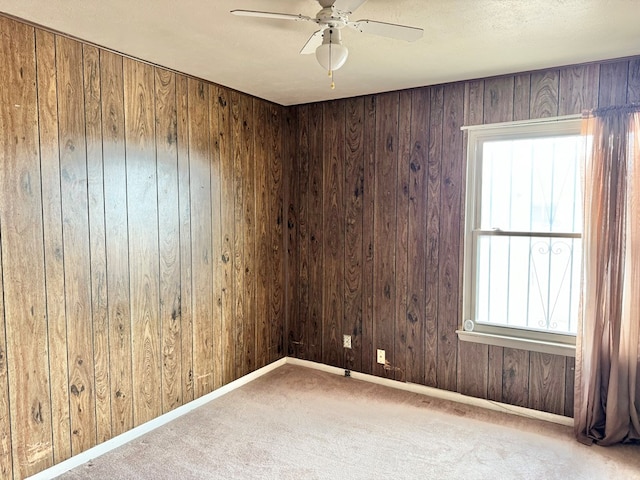 carpeted spare room featuring ceiling fan and wood walls