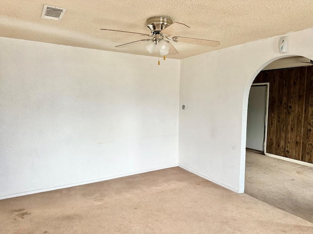 carpeted spare room featuring ceiling fan, a textured ceiling, and wooden walls