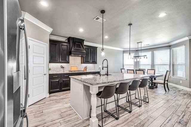 6003 Sunny Stone Dr, Midland, TX 79705 - kitchen with appliances with stainless steel finishes, premium range hood, light wood-style flooring, ornamental molding, and a breakfast bar area