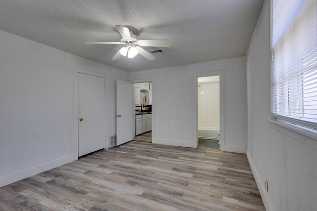 107 W 10th St, Big Spring, TX 79720 - unfurnished bedroom featuring light wood finished floors, a textured ceiling, ensuite bath, and a ceiling fan