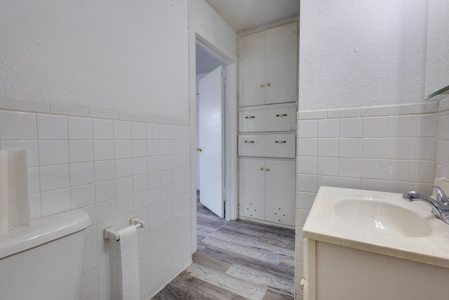 107 W 10th St, Big Spring, TX 79720 - bathroom featuring tile walls, vanity, wood finished floors, wainscoting, and a textured wall