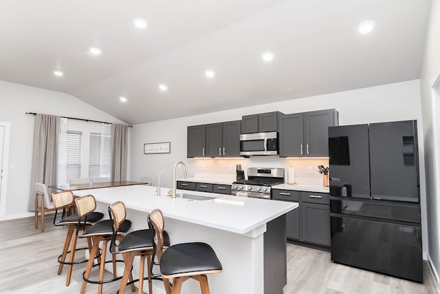 kitchen featuring stainless steel appliances, vaulted ceiling, a sink, a kitchen breakfast bar, and light wood finished floors