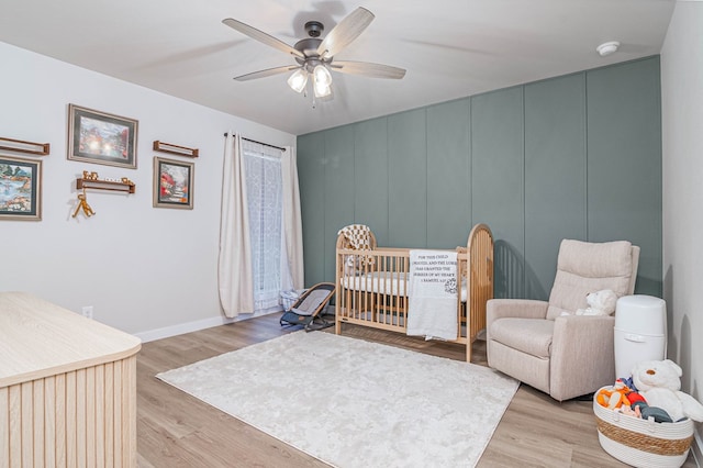 bedroom with a nursery area, light wood finished floors, ceiling fan, and baseboards