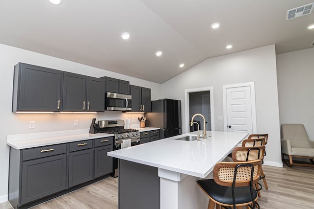 kitchen featuring appliances with stainless steel finishes, a sink, light wood-type flooring, a kitchen island with sink, and lofted ceiling