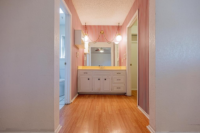 hallway featuring a textured wall, a sink, a textured ceiling, and light wood finished floors