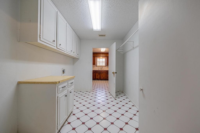 clothes washing area featuring light floors, visible vents, cabinet space, a sink, and a textured ceiling