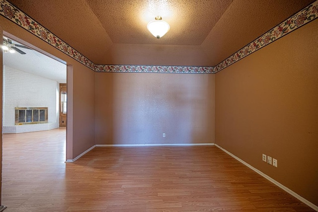 empty room featuring a textured ceiling, a fireplace, baseboards, and wood finished floors