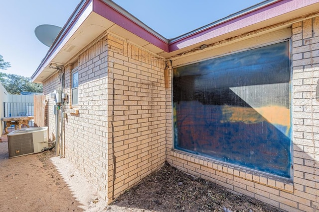 view of side of home featuring brick siding, fence, and central AC unit