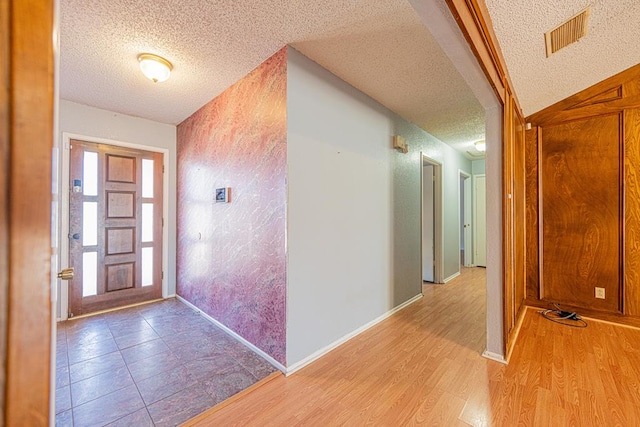 entrance foyer with a textured ceiling, light wood finished floors, visible vents, and baseboards