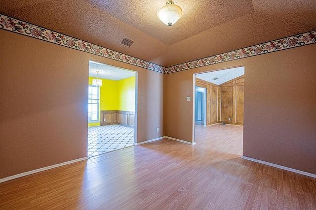 spare room featuring a textured ceiling, visible vents, wood finished floors, and wainscoting