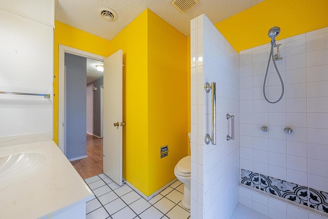 full bathroom with visible vents, a tile shower, a textured ceiling, and vanity