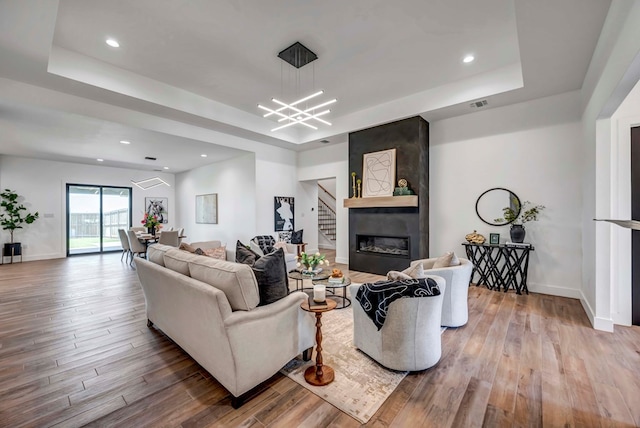 living room featuring a raised ceiling, a fireplace, and light wood-type flooring