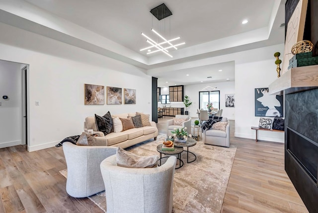 living room with a raised ceiling, a notable chandelier, and light hardwood / wood-style flooring