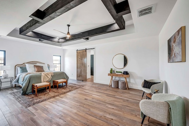 bedroom featuring a raised ceiling, a barn door, and light wood-type flooring