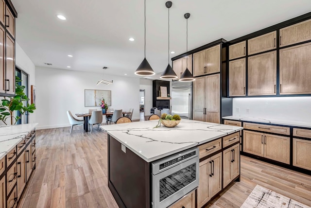 kitchen featuring a center island, hanging light fixtures, light wood-type flooring, stainless steel microwave, and light stone countertops