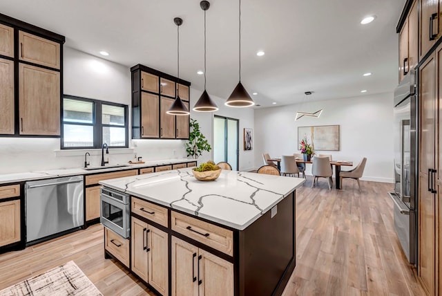 kitchen with sink, stainless steel appliances, a center island, light stone counters, and decorative light fixtures