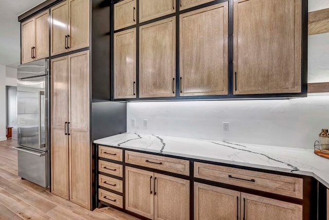 kitchen featuring stainless steel built in refrigerator, light stone countertops, and light wood-type flooring