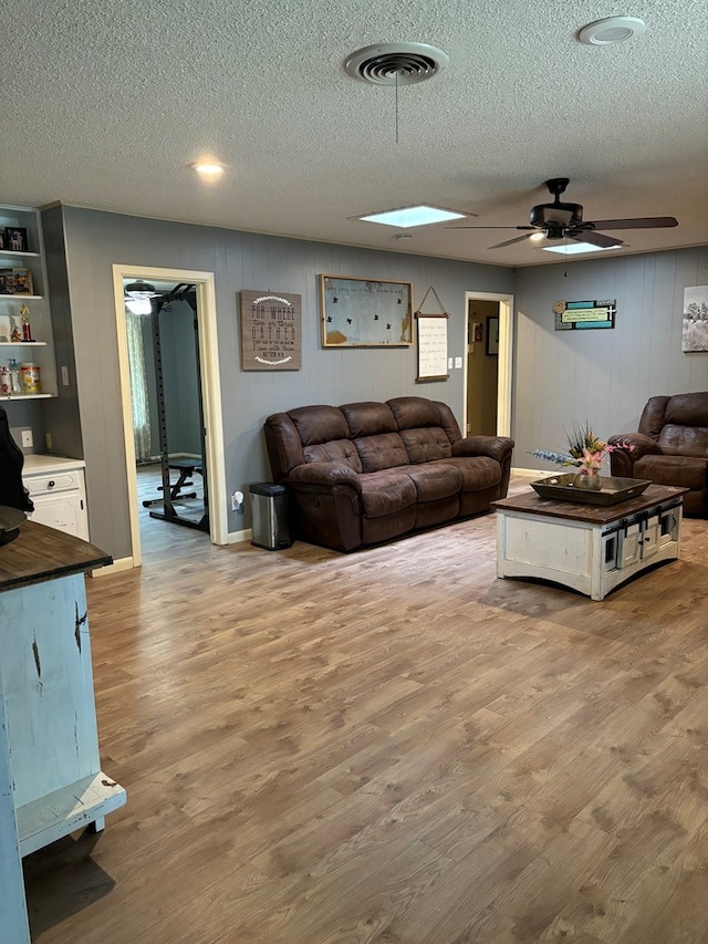 living room with a textured ceiling, light wood-type flooring, a skylight, and ceiling fan