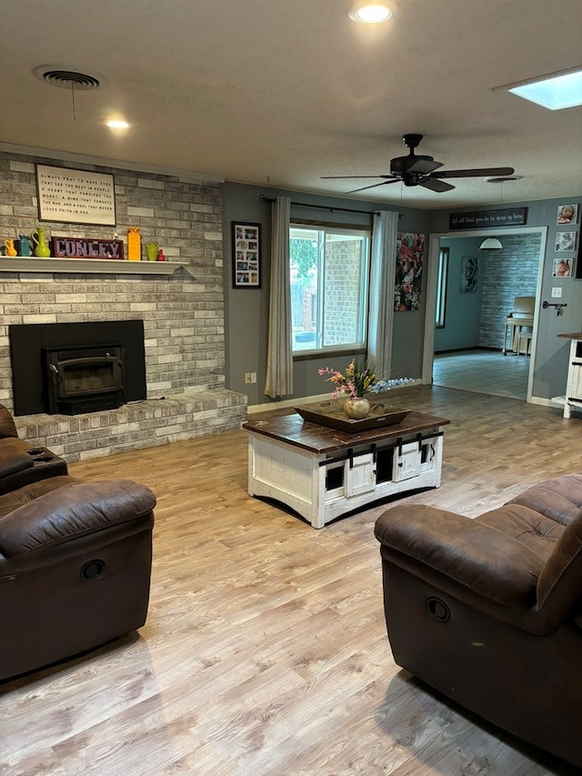 living room with ceiling fan, a skylight, a textured ceiling, and light hardwood / wood-style flooring