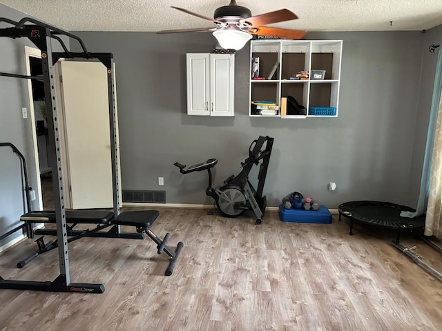 exercise area with ceiling fan, a textured ceiling, and light wood-type flooring