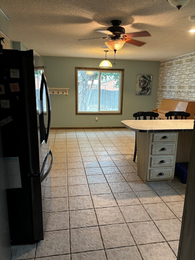 kitchen featuring black refrigerator, a kitchen breakfast bar, a textured ceiling, ceiling fan, and light tile patterned floors