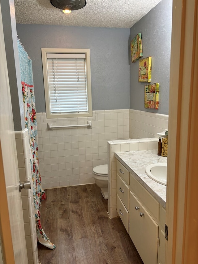 bathroom with a textured ceiling, hardwood / wood-style floors, vanity, and tile walls