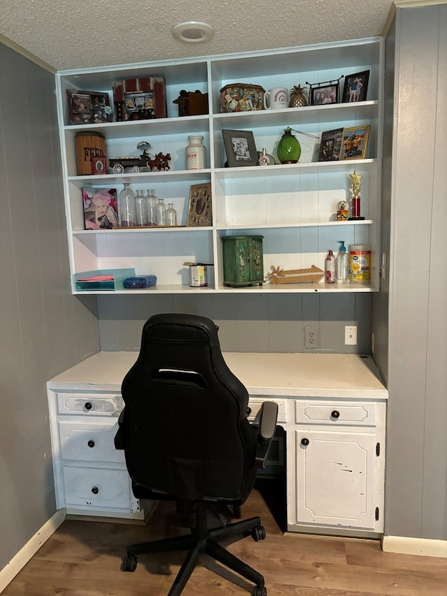 office with light wood-type flooring, a textured ceiling, built in desk, and wood walls