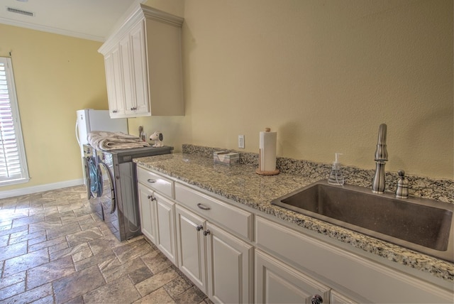 clothes washing area featuring cabinets, crown molding, sink, and washing machine and clothes dryer