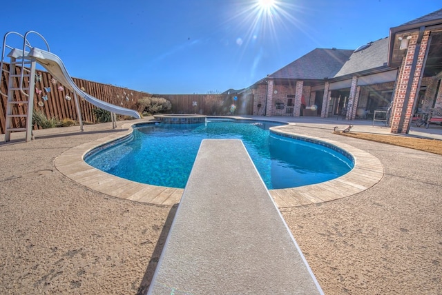 view of pool featuring a jacuzzi, a water slide, a diving board, and a patio