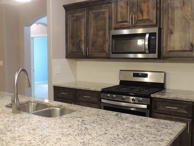 kitchen with tasteful backsplash, light stone counters, sink, and appliances with stainless steel finishes