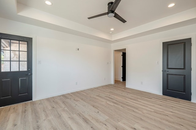 foyer entrance with ceiling fan, a tray ceiling, and light hardwood / wood-style flooring