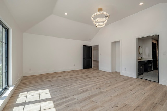 unfurnished bedroom featuring ensuite bathroom, high vaulted ceiling, a chandelier, and light hardwood / wood-style flooring