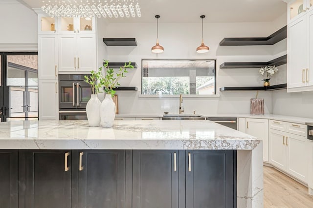 kitchen with sink, white cabinetry, light stone counters, decorative light fixtures, and light hardwood / wood-style flooring