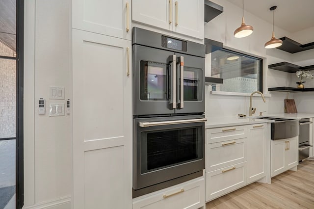 kitchen with sink, light wood-type flooring, pendant lighting, stainless steel double oven, and white cabinets