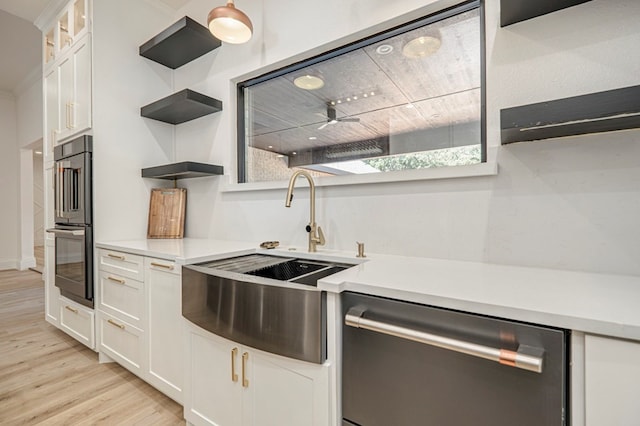 kitchen with multiple ovens, sink, white cabinets, stainless steel dishwasher, and light hardwood / wood-style floors