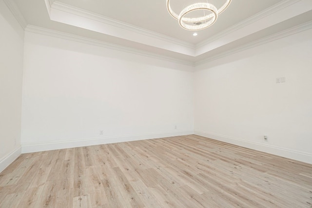 spare room with crown molding, a tray ceiling, a chandelier, and light wood-type flooring