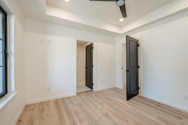 unfurnished bedroom with connected bathroom, a tray ceiling, and light hardwood / wood-style flooring